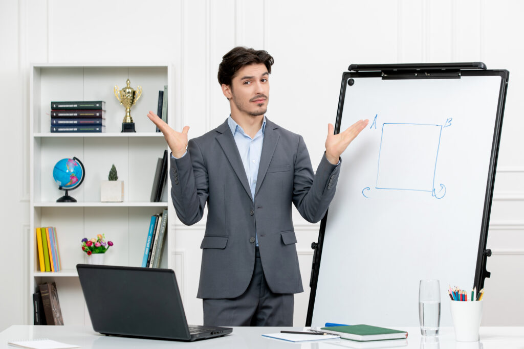 The current image has no alternative text. The file name is: teacher-smart-instructor-grey-suit-classroom-with-computer-whiteboard-waving-hands-scaled.jpg